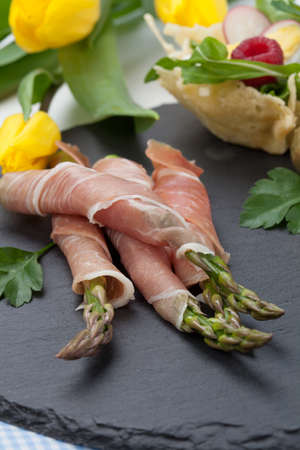 Grilled asparagus wrapped in prosciutto and parmesan baskets filled with fresh garden salad. Easter decorated eggs, tulips flowers, holiday theme.の写真素材