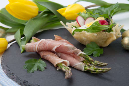 Grilled asparagus wrapped in prosciutto and parmesan baskets filled with fresh garden salad. Easter decorated eggs, tulips flowers, holiday theme.の写真素材