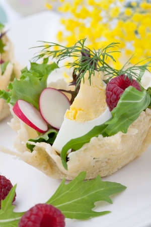 Parmesan baskets filled with fresh garden salad, hard-boiled eggs, and fresh raspberries. Easter decorated eggs, spring flowers, holiday theme. Over white.の写真素材