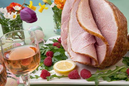 Easter themed prepared sliced honey ham and fresh raspberry, arugula, lemons, Ester eggs decoration. Spring flowers and pink wine.の写真素材