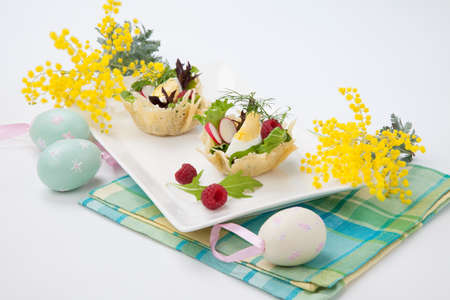 Parmesan baskets filled with fresh garden salad, hard-boiled eggs, and fresh raspberries. Easter decorated eggs, spring flowers, holiday theme. Over white.の写真素材