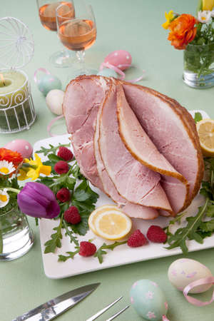 Easter themed prepared sliced honey ham and fresh raspberry, arugula, lemons, Ester eggs decoration. Spring flowers and pink wine.の写真素材