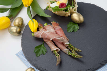 Grilled asparagus wrapped in prosciutto and parmesan baskets filled with fresh garden salad. Easter decorated eggs, tulips flowers, holiday theme.の写真素材
