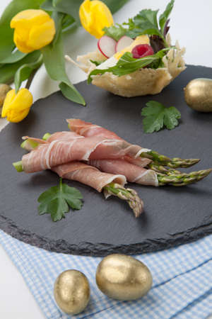 Grilled asparagus wrapped in prosciutto and parmesan baskets filled with fresh garden salad. Easter decorated eggs, tulips flowers, holiday theme.の写真素材
