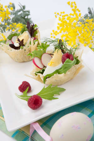 Parmesan baskets filled with fresh garden salad, hard-boiled eggs, and fresh raspberries. Easter decorated eggs, spring flowers, holiday theme. Over white.の写真素材