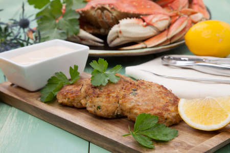 Three crab cakes appetizer with spicy sauce and fresh parsley. Dungeness crab in the background.の写真素材