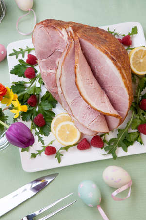 Easter themed prepared sliced honey ham and fresh raspberry, arugula, lemons, Ester eggs decoration. Spring flowers and pink wine.の写真素材