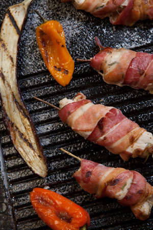 Grilled bacon-wrapped chicken tenders with lemon and rosemary on the grill wih grilled vegetables - peppers, and and eggplant.の写真素材