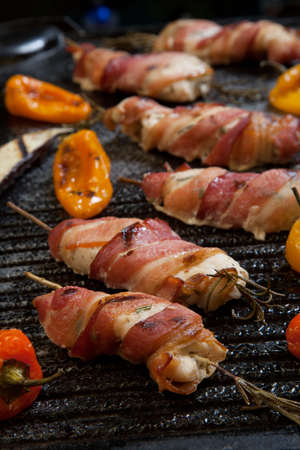 Grilled bacon-wrapped chicken tenders with lemon and rosemary on the grill wih grilled vegetables - peppers, and and eggplant.の写真素材