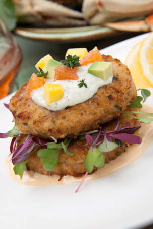 Crab cakes appetizer with two sauces, baby greens, and mango - avocado citrus salsa. Dungeness crab in the background.の写真素材