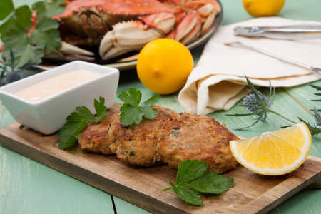 Three crab cakes appetizer with spicy sauce and fresh parsley. Dungeness crab in the background.の写真素材