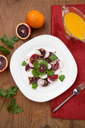 Closeup of a plate of juicy salad with blood oranges, radish, spinach, and pumpkin seeds. Citrus dressing.の写真素材