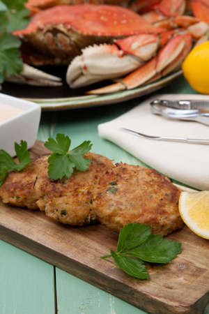 Three crab cakes appetizer with spicy sauce and fresh parsley. Dungeness crab in the background.の写真素材