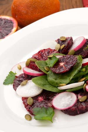 Closeup of a plate of juicy salad with blood oranges, radish, spinach, and pumpkin seeds. Citrus dressing.の写真素材