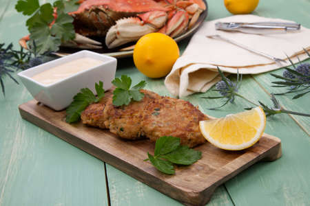 Three crab cakes appetizer with spicy sauce and fresh parsley. Dungeness crab in the background.の写真素材