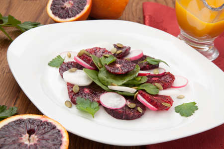Closeup of a plate of juicy salad with blood oranges, radish, spinach, and pumpkin seeds. Citrus dressing.の写真素材