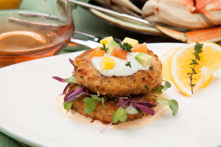 Crab cakes appetizer with two sauces, baby greens, and mango - avocado citrus salsa. Dungeness crab in the background.の写真素材