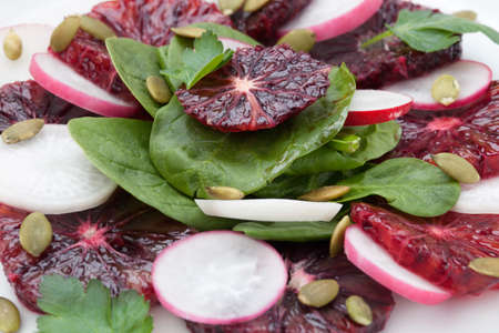 Closeup of a plate of juicy salad with blood oranges, radish, spinach, and pumpkin seeds. Citrus dressing.の写真素材