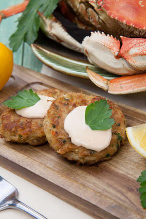 Three crab cakes appetizer with spicy sauce and fresh parsley. Dungeness crab in the background.の写真素材