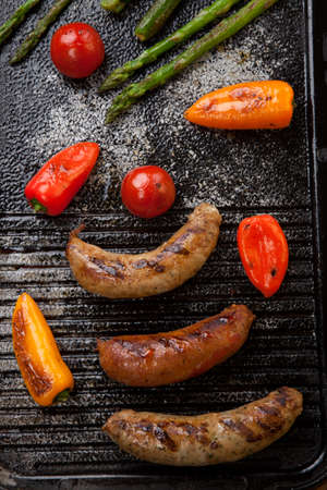 Summer grill - grilled sausages and assorted grilled vegetables - asparagus, mini pepper, and tomatoes - on griddle.の写真素材