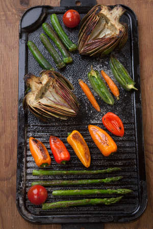 Assorted grilled vegetables - zucchini, asparagus, artichokes, mini pepper, jalapeno, tomatoes, and carrots - on griddle.の写真素材