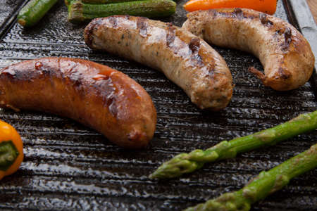Summer grill - grilled sausages and assorted grilled vegetables - asparagus, mini pepper, and tomatoes - on griddle.の写真素材