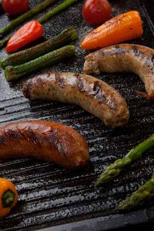 Summer grill - grilled sausages and assorted grilled vegetables - asparagus, mini pepper, and tomatoes - on griddle.の写真素材