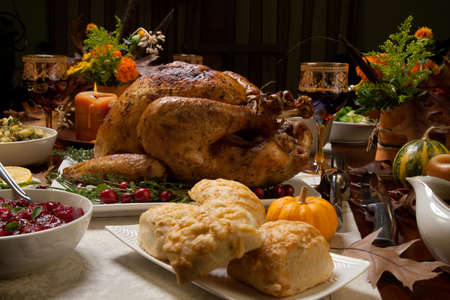 Roasted turkey garnished with cranberries on a rustic style table decoraded with pumpkins, gourds, asparagus, brussel sprouts, baked vegetables, pie, flowers, and candles.の写真素材