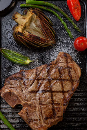 Summer grill - grilled T-bone steak and assorted grilled vegetables - asparagus, mini pepper, and tomatoes - on griddle.の写真素材