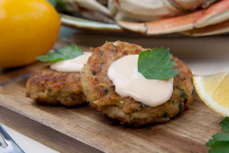 Three crab cakes appetizer with spicy sauce and fresh parsley. Dungeness crab in the background.の写真素材