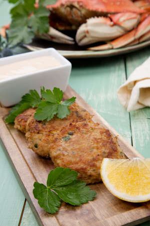 Three crab cakes appetizer with spicy sauce and fresh parsley. Dungeness crab in the background.の写真素材