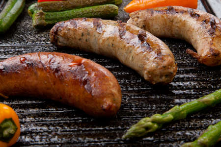 Summer grill - grilled sausages and assorted grilled vegetables - asparagus, mini pepper, and tomatoes - on griddle.の写真素材