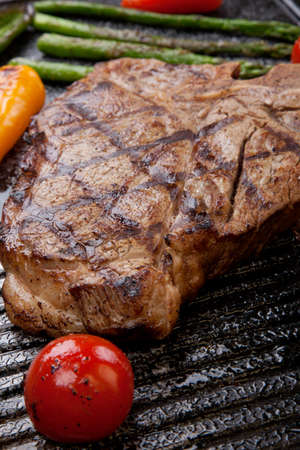 Summer grill - grilled T-bone steak and assorted grilled vegetables - asparagus, mini pepper, and tomatoes - on griddle.の写真素材