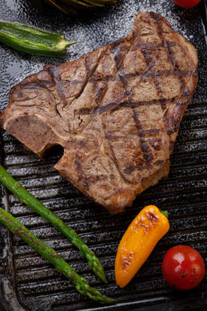 Summer grill - grilled T-bone steak and assorted grilled vegetables - asparagus, mini pepper, and tomatoes - on griddle.の写真素材