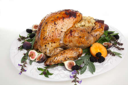 Glazed roasted turkey on serving tray over white background. Garnished with figs, blackberry, persimmon, sage, and basil.の写真素材