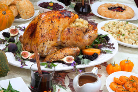Dinner table with roasted Thanksgiving turkey is ready to feast. Turkey is garnished with fresh figs, blackberries, sage, and basil. Sided dishes, pumpkinks, flowers, and red wine cocktails.の写真素材