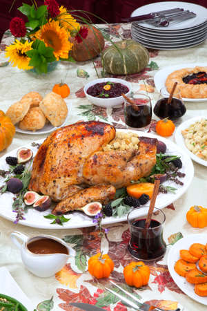 Dinner table with roasted Thanksgiving turkey is ready to feast. Turkey is garnished with fresh figs, blackberries, sage, and basil. Sided dishes, pumpkinks, flowers, and red wine cocktails.の写真素材