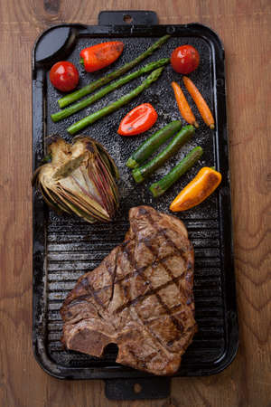 Summer grill - grilled T-bone steak and assorted grilled vegetables - asparagus, mini pepper, and tomatoes - on griddle.の写真素材