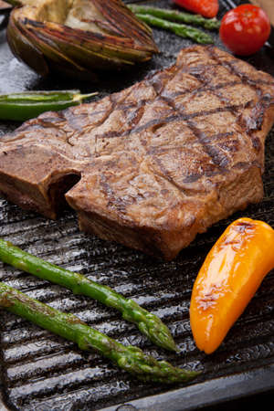 Summer grill - grilled T-bone steak and assorted grilled vegetables - asparagus, mini pepper, and tomatoes - on griddle.の写真素材