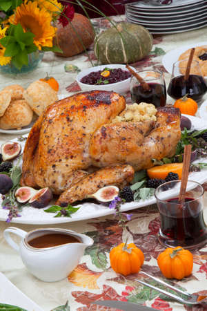 Dinner table with roasted Thanksgiving turkey is ready to feast. Turkey is garnished with fresh figs, blackberries, sage, and basil. Sided dishes, pumpkinks, flowers, and red wine cocktails.の写真素材