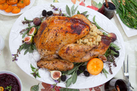 Dinner table with roasted Thanksgiving turkey is ready to feast. Turkey is garnished with fresh figs, blackberries, sage, and basil. Sided dishes, pumpkinks, flowers, and red wine cocktails.の写真素材