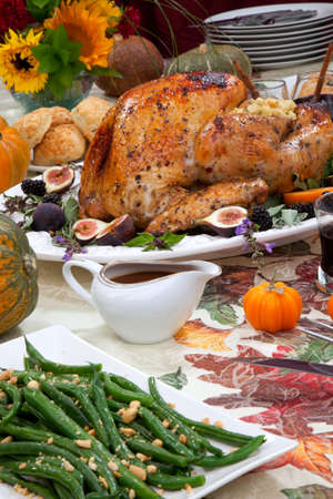Dinner table with roasted Thanksgiving turkey is ready to feast. Turkey is garnished with fresh figs, blackberries, sage, and basil. Sided dishes, pumpkinks, flowers, and red wine cocktails.の写真素材