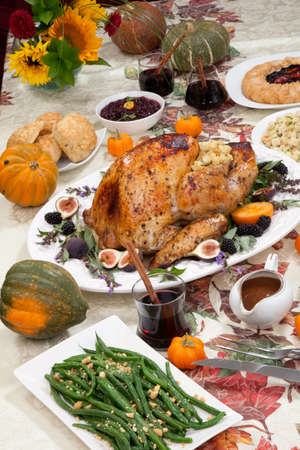 Dinner table with roasted Thanksgiving turkey is ready to feast. Turkey is garnished with fresh figs, blackberries, sage, and basil. Sided dishes, pumpkinks, flowers, and red wine cocktails.の写真素材