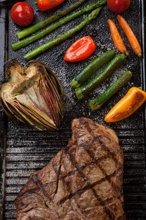 Summer grill - grilled T-bone steak and assorted grilled vegetables - asparagus, mini pepper, and tomatoes - on griddle.の写真素材