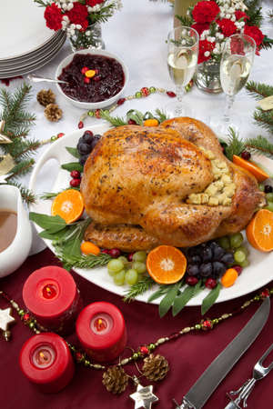 Roasted herb rubbed turkey garnished with fresh grapes, oranges, and cranberry is ready for Christmas dinner. Ornaments, Champagne, candles, and other Christmas decorations on feast table.の写真素材