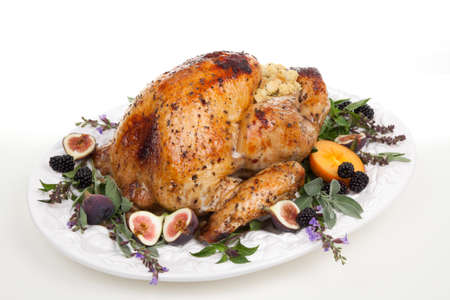 Glazed roasted turkey on serving tray over white background. Garnished with figs, blackberry, persimmon, sage, and basil.の写真素材