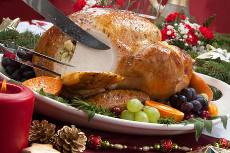 Carving roasted herb rubbed turkey garnished with fresh grapes, oranges, and cranberry is ready for Christmas dinner. Ornaments, Champagne, candles, and other Christmas decorations on feast table.の写真素材