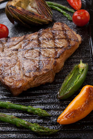 Summer grill - grilled T-bone steak and assorted grilled vegetables - asparagus, mini pepper, and tomatoes - on griddle.の写真素材