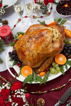 Roasted herb rubbed turkey garnished with fresh grapes, oranges, and cranberry is ready for Christmas dinner. Ornaments, Champagne, candles, and other Christmas decorations on feast table.の写真素材