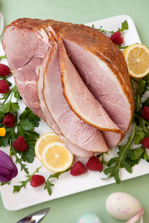 Easter themed prepared sliced honey ham and fresh raspberry, arugula, lemons, Ester eggs decoration. Spring flowers and pink wine.の写真素材